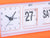 Närbild av en orange väckarklocka med bläddernummer, datum 27 och visare
