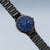Bering Herren-Solaruhr am Handgelenk, schwarzes Kettenarmband und blaues Zifferblatt sichtbar.