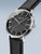 Herrenuhr seitlich schräg: schwarzes Zifferblatt, silbernes Gehäuse, schwarzes Lederarmband