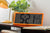 Retro LCD-väggklocka i neonorange på bord med digital visning av tid och datum