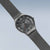 Herrenarmbanduhr mit grauem Milanaiseband, rundem Gehäuse und dunklem Zifferblatt
