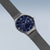 Herrenarmbanduhr im Profil: graues Gehäuse, dunkelblaues Zifferblatt, Milanaise-Armband