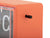 Orangefärgad väggklocka med transparent ram och vred på sidan