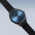 Armbanduhr mit blauem Zifferblatt, schwarzem Mesh-Band und runder Lünette.
