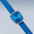 Damenuhr mit blauem Zifferblatt, silbernem Gehäuse und blauem Textilarmband, quadratisches Profil.