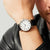 Herrenuhr am Handgelenk: weißes Zifferblatt, schwarze Lederarmband-Schließe, silbernes Gehäuse