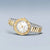 Damenuhr seitlich mit Gold-Details, weißem Zifferblatt und zweifarbigem Metallarmband
