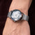 Silberne Damenarmbanduhr am Handgelenk mit Metallarmband und rundem Perlmutt-Blütenzifferblatt