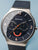 Bering Herrenuhr mit blauem Zifferblatt, orangefarbenen Akzenten und Milanaise-Armband