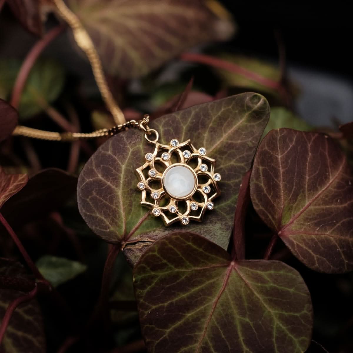 Gyllene halsband med rund, vit cabochon i blommigt hänge med gnistrande stenar