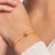 Guldpläterat armband runt handleden med vita stenar och ett litet hänge