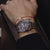 Herrklocka på handleden med silverfärgat metallarmband och svart urtavla