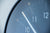 Detail einer runden Wanduhr: dunkelblaues Zifferblatt, weiße Zeiger, goldene Akzente