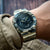 Herrenarmbanduhr mit Tarnmusterband am Handgelenk, schwarzes Zifferblatt im Blick