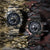 Zwei Herrenarmbanduhren mit Tarnmusterbändern und schwarzen Zifferblättern nebeneinander