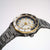 Herrenuhr schräg von oben: dunkles Metallarmband, schwarzes Zifferblatt mit goldener Lünette.