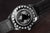 Klockfodral bakifrån med världskartmotiv i ringen och svart läderband