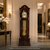 Standuhr aus dunklem Holz mit geschwungenem Aufsatz, goldfarbenen Pendelstäben und Uhrwerk