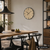 Wanduhr mit Holz-Zifferblatt, Metallring und schwarzen Zeigern an weißer Wand